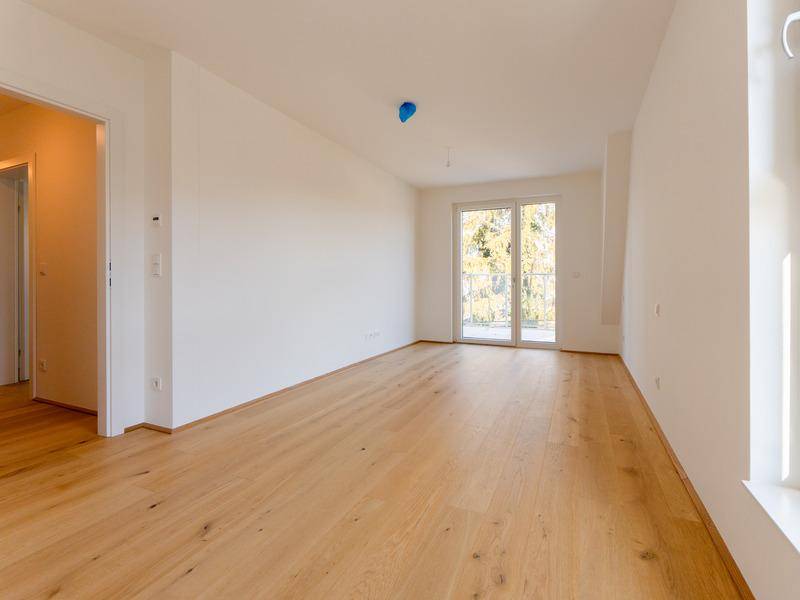 Heller, leerer Raum mit Holzboden und Zugang zu einem Balkon, ideal als Schlaf- oder Wohnzimmer.