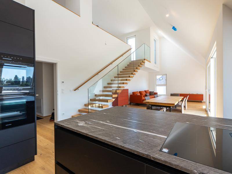 Moderne Küche mit integrierten Geräten und Blick auf den offenen Wohnbereich mit Treppe.