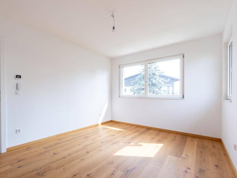 Helles Schlafzimmer mit Eichenparkettboden und einem Fenster mit Blick ins Grüne.