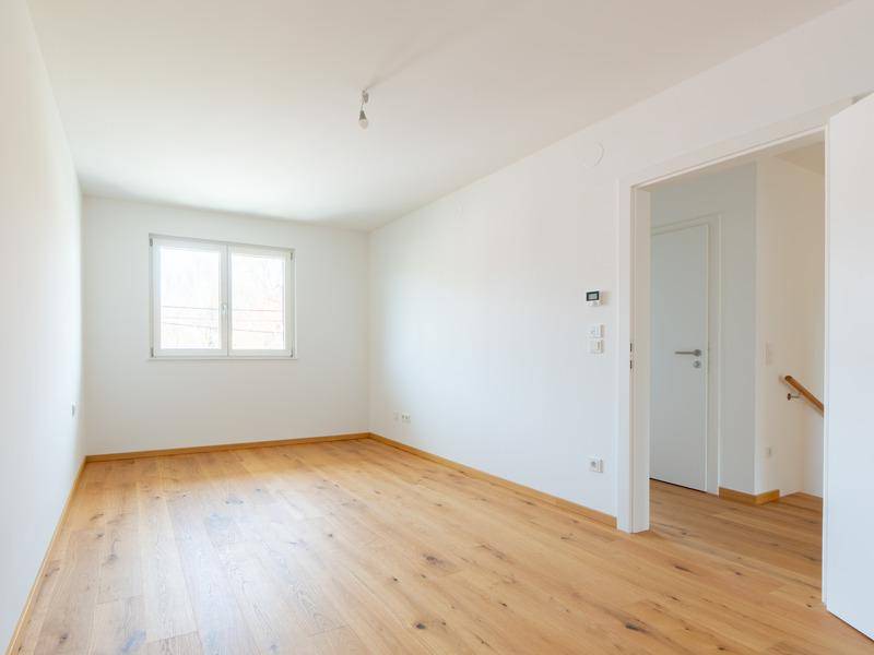 Leeres Zimmer mit Eichenparkettboden und viel Tageslicht durch das Fenster.