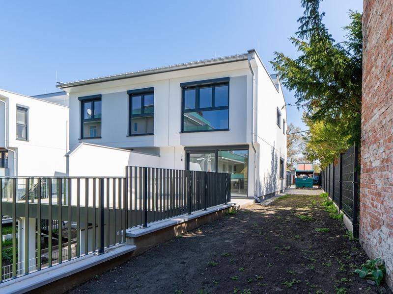 Moderne Hausfassade mit dunklen Fenstern und einem ungestalteten Gartenbereich.