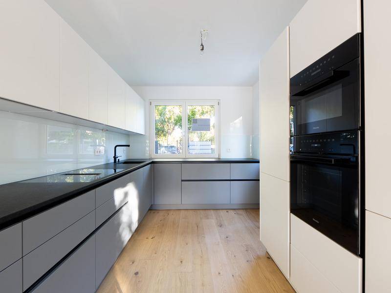 Moderne Küche mit weißen und grauen Fronten, dunkler Arbeitsplatte und Einbaugeräten.
