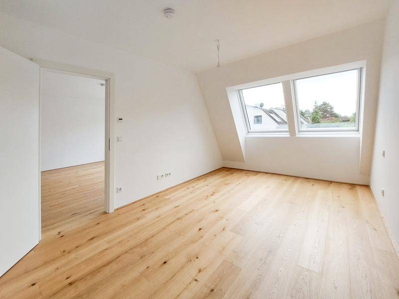 Helles Zimmer im Dachgeschoss mit Holzplankenboden und schrägen Dachfenstern.