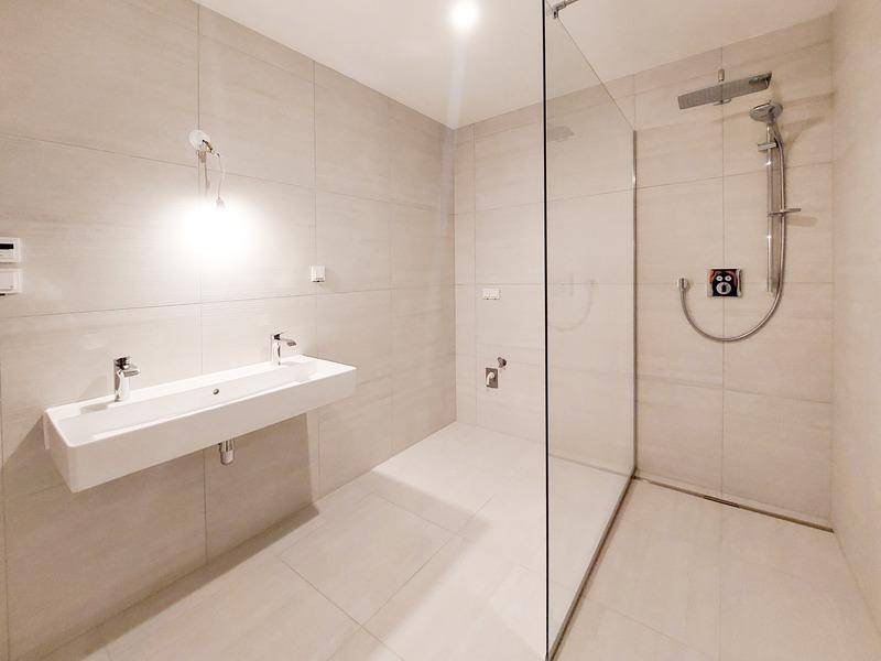 Modernes Badezimmer mit hellen Fliesen, wandhängendem Waschbecken und begehbarer Dusche.