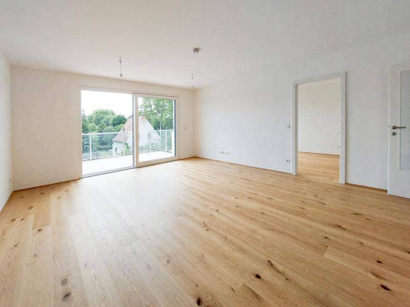 Lichtdurchfluteter Wohnraum mit Holzplankenboden und großem Schiebetürzugang zum Balkon.