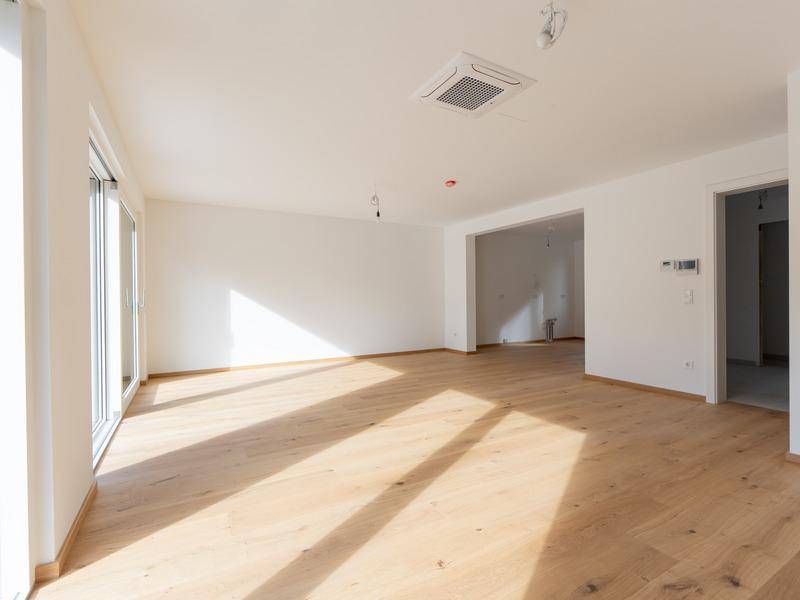 Geräumiges Wohnzimmer mit Holzboden, offener Raumgestaltung und integrierter Klimaanlage.