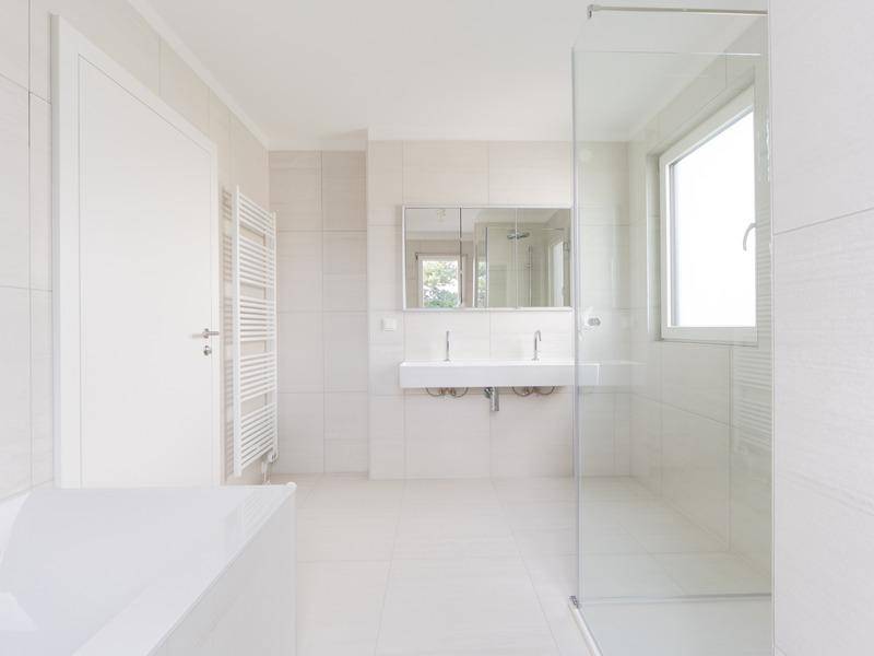 Modernes Badezimmer mit weißen Fliesen, Doppelwaschbecken, Badewanne und Duschbereich.