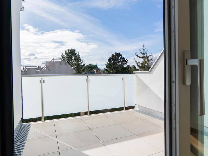 Moderner Balkon mit Fliesenboden und Glasgeländer unter blauem Himmel.