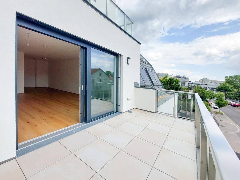 Moderner Balkon mit Fliesenboden und Glasgeländer, mit Zugang zu einem hellen Innenraum.