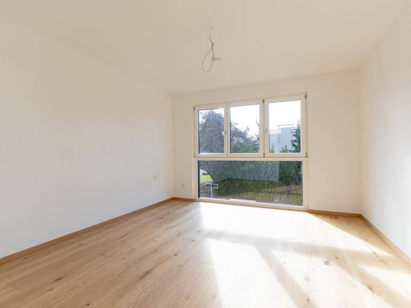 Helles Schlafzimmer mit Eichenparkett und großem Fenster mit Blick ins Grüne.
