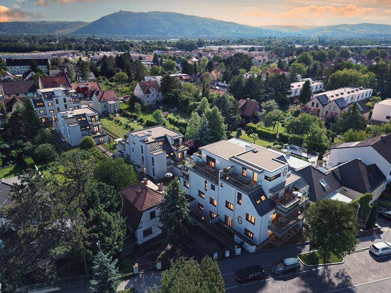Abendliche Luftaufnahme einer Wohnsiedlung mit modernen Gebäuden und Bergblick in der Ferne.