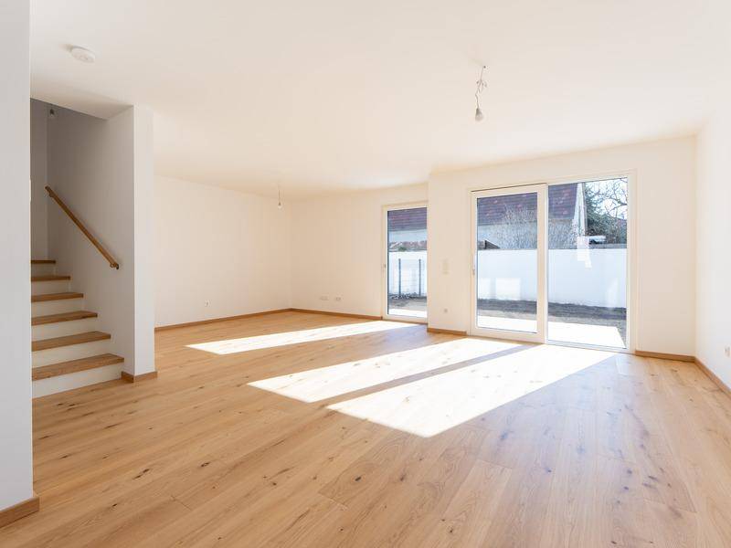 Lichtdurchfluteter Wohnbereich mit Holzboden, Zugang zur Terrasse und offener Treppe.
