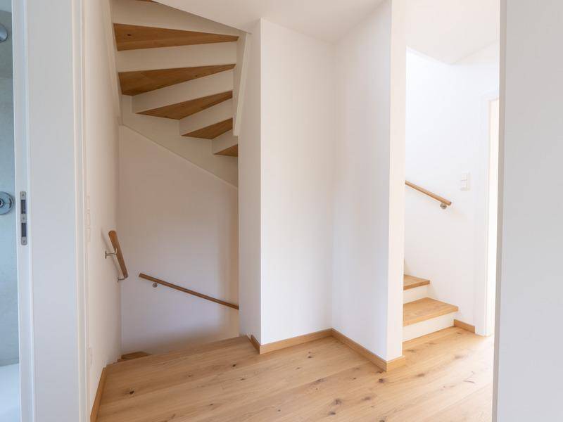Heller Flurbereich mit Holztreppe und schlichten weißen Wänden.