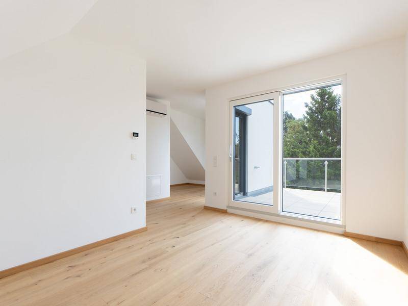 Heller Raum mit Holzboden, Dachschräge und Zugang zu einem Balkon oder einer Terrasse.