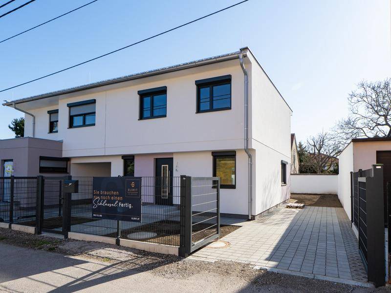 Moderne Hausfassade mit großen Fenstern, Rollläden und einem gepflegten Vorgartenbereich.