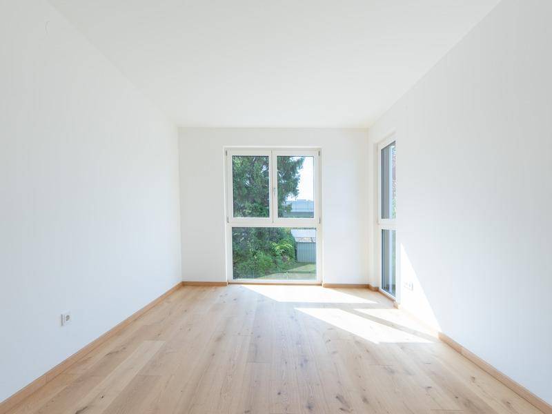 Helles Zimmer mit Holzboden und großem Fenster mit Blick ins Grüne.