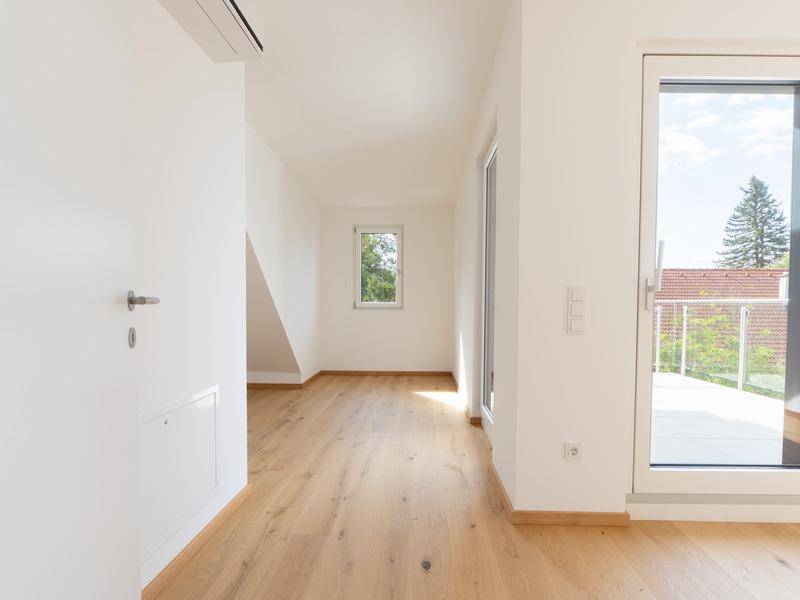 Heller Flur mit Holzboden, Dachschräge und Fenster, das Tageslicht hereinlässt.