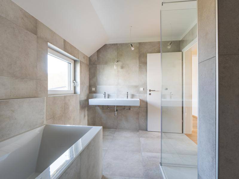 Modernes Badezimmer mit grauen Fliesen, Doppelwaschbecken, Badewanne und Dusche.