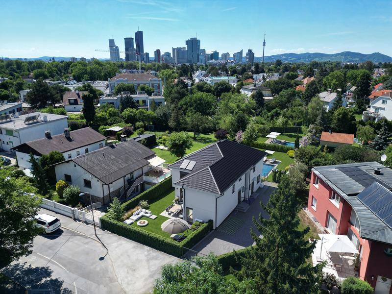 Luftaufnahme eines Wohnhauses mit Pool und Garten, umgeben von Grünflächen und Stadtblick.
