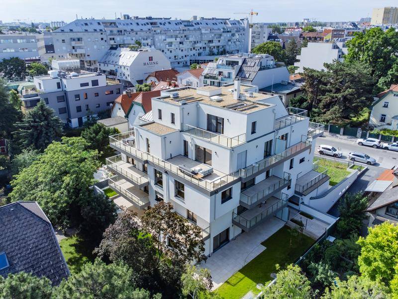 Panoramablick auf ein modernes Wohngebäude mit großzügigen Balkonen und Dachterrassen, umgeben von Grünflächen.