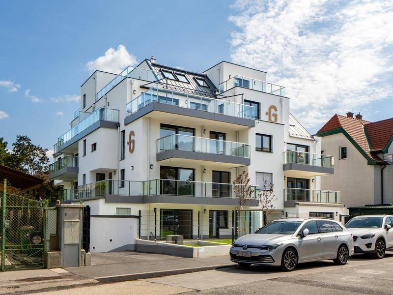 Modernes Apartmentgebäude mit mehreren Balkonen und Glasgeländern unter blauem Himmel.