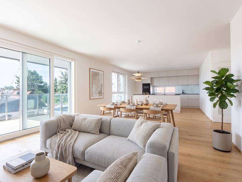 Helles, offenes Wohn-Esszimmer mit moderner Küche, Holzboden und Zugang zum Balkon.