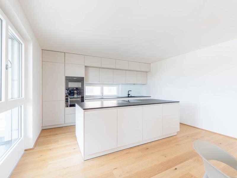 Moderne, helle Küche mit weißer Kücheninsel, Einbaugeräten und Holzboden.