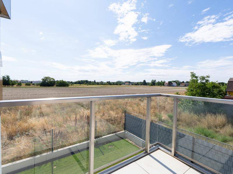 Balkon mit Blick auf weite Felder und grüne Landschaft unter blauem Himmel.