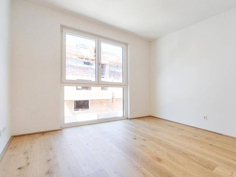 Helles Schlafzimmer mit großem Fenster und Holzboden, Blick auf die Baustelle nebenan.