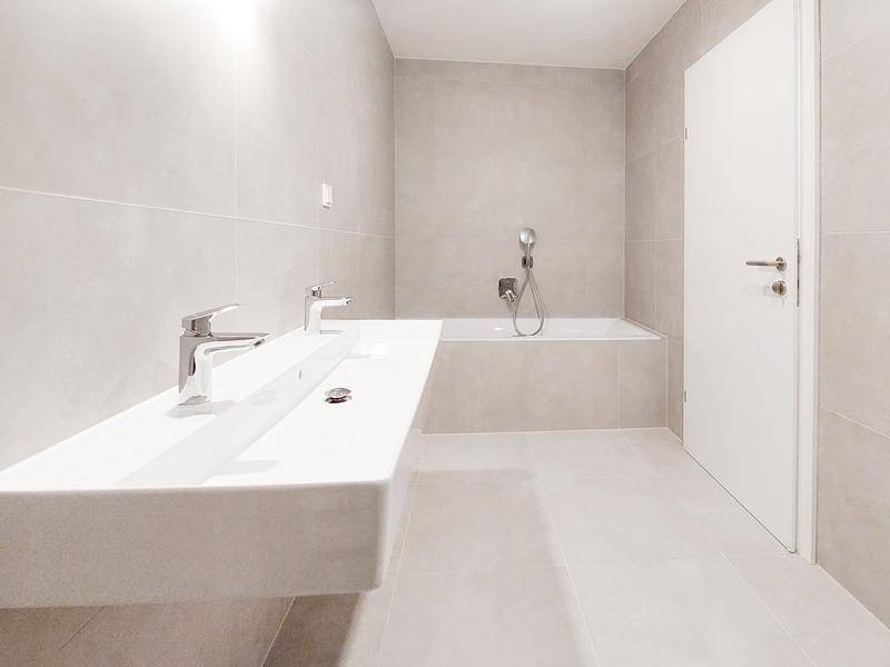 Modernes Badezimmer mit Badewanne, Einzelwaschbecken und hellen, großformatigen Fliesen.