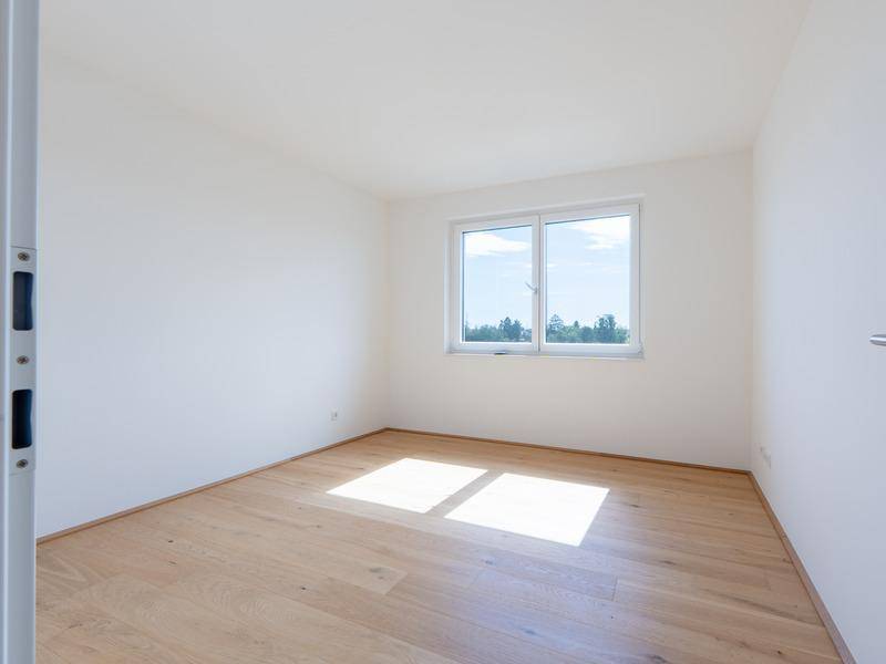 Lichtdurchflutetes Schlafzimmer mit Holzboden und weiß gestrichenen Wänden, sehr hell.