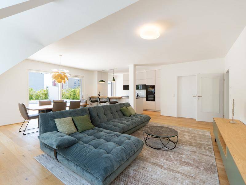 Heller offener Wohn-Essbereich mit modernem Sofa, Holzboden und integrierter Küche.
