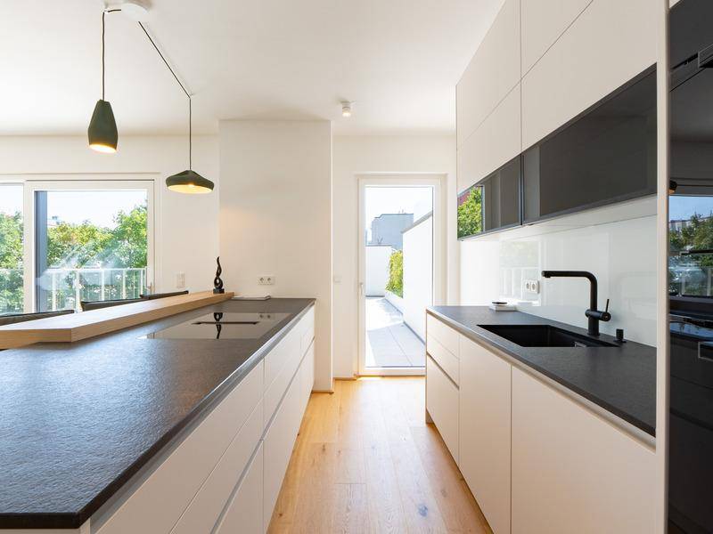 Moderne Küche mit weißen Schränken, dunklen Arbeitsplatten und Kochinsel mit Zugang zur Terrasse.
