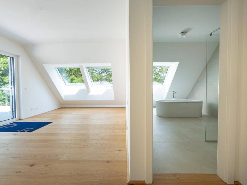 Heller Raum mit Holzboden, großen Dachfenstern und Blick auf ein angrenzendes Badezimmer.