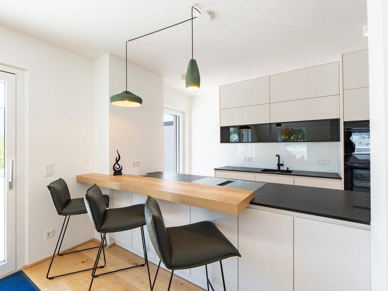 Moderne Küche mit Frühstücksbar, Barhockern und stilvollen grünen Pendelleuchten.