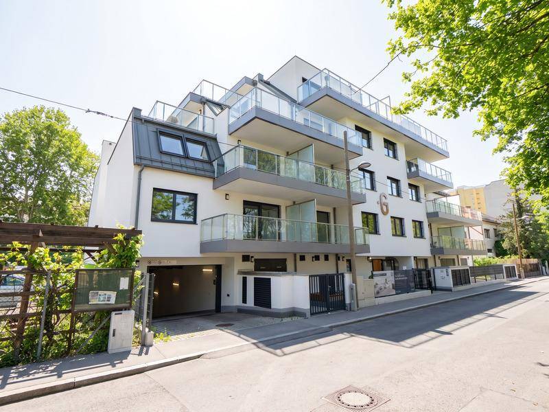Modernes Mehrfamilienhaus mit mehreren Balkonen, Glasgeländern und Tiefgaragenzufahrt.