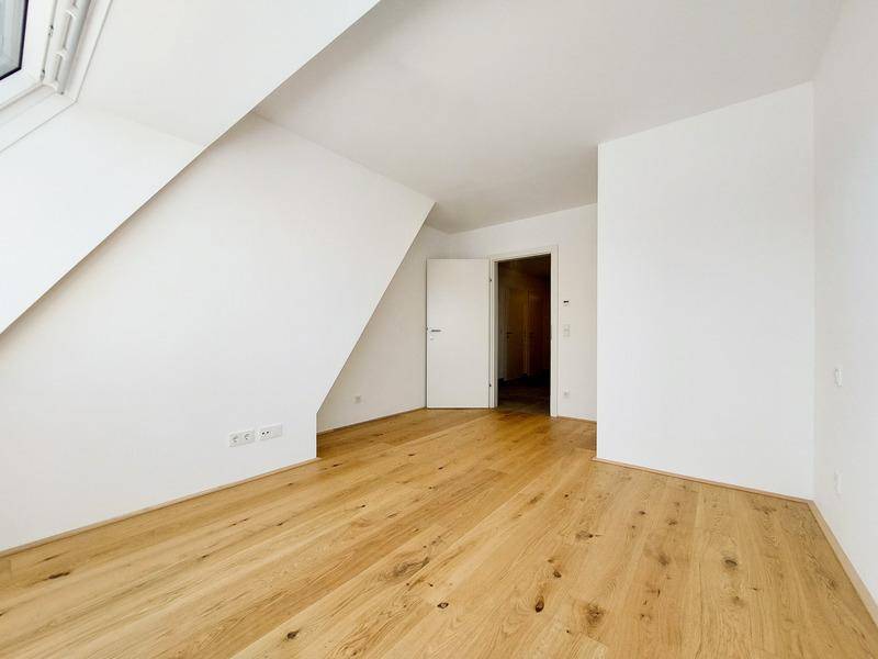 Helles Schlafzimmer mit Dachschräge und Holzboden, bietet Potenzial für gemütliche Einrichtung.