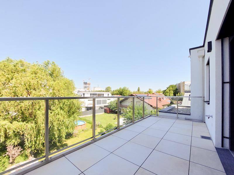 Geräumiger Balkon mit Fliesenboden und Glasgeländer, bietet Blick auf grüne Umgebung.