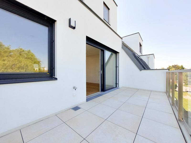 Heller Balkon mit Fliesenboden und Glasgeländer, bietet Zugang zu einem Innenraum.