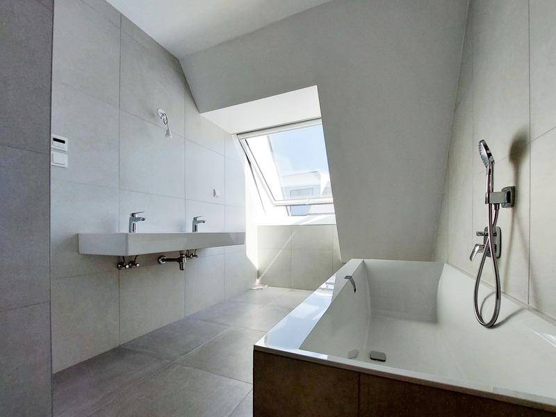 Modernes Badezimmer mit Badewanne, Doppelwaschbecken und Dachfenster für viel Tageslicht.