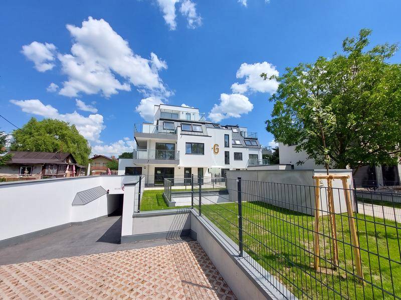 Moderne Wohnanlage mit weißer Fassade, Tiefgaragenzufahrt und gepflegter Außenanlage.
