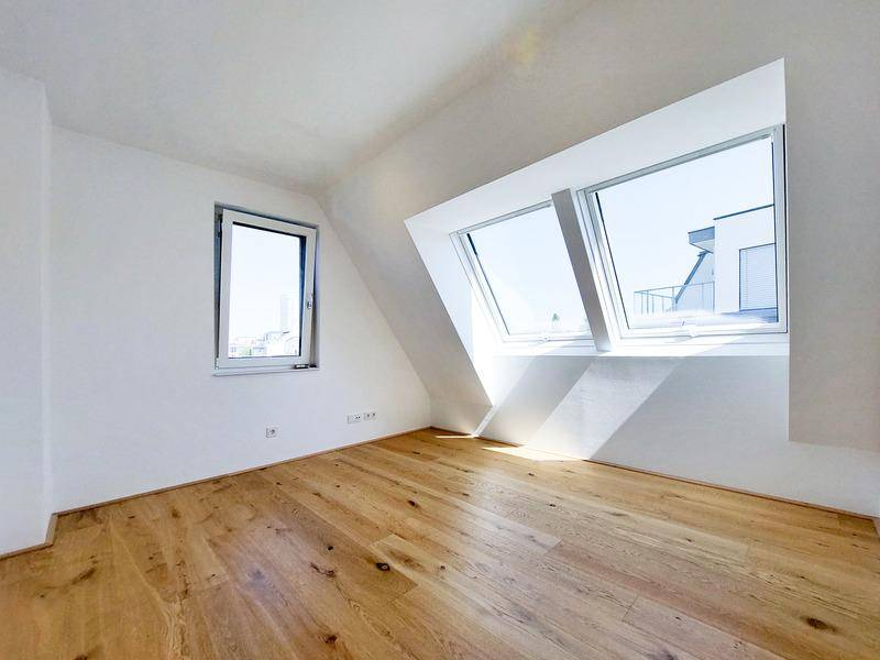 Geräumiges Zimmer im Dachgeschoss mit Holzboden, Dachfenstern und einem zusätzlichen Seitenfenster.