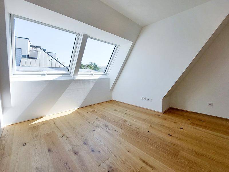 Helles Zimmer im Dachgeschoss mit Holzboden und zwei großen Dachfenstern.