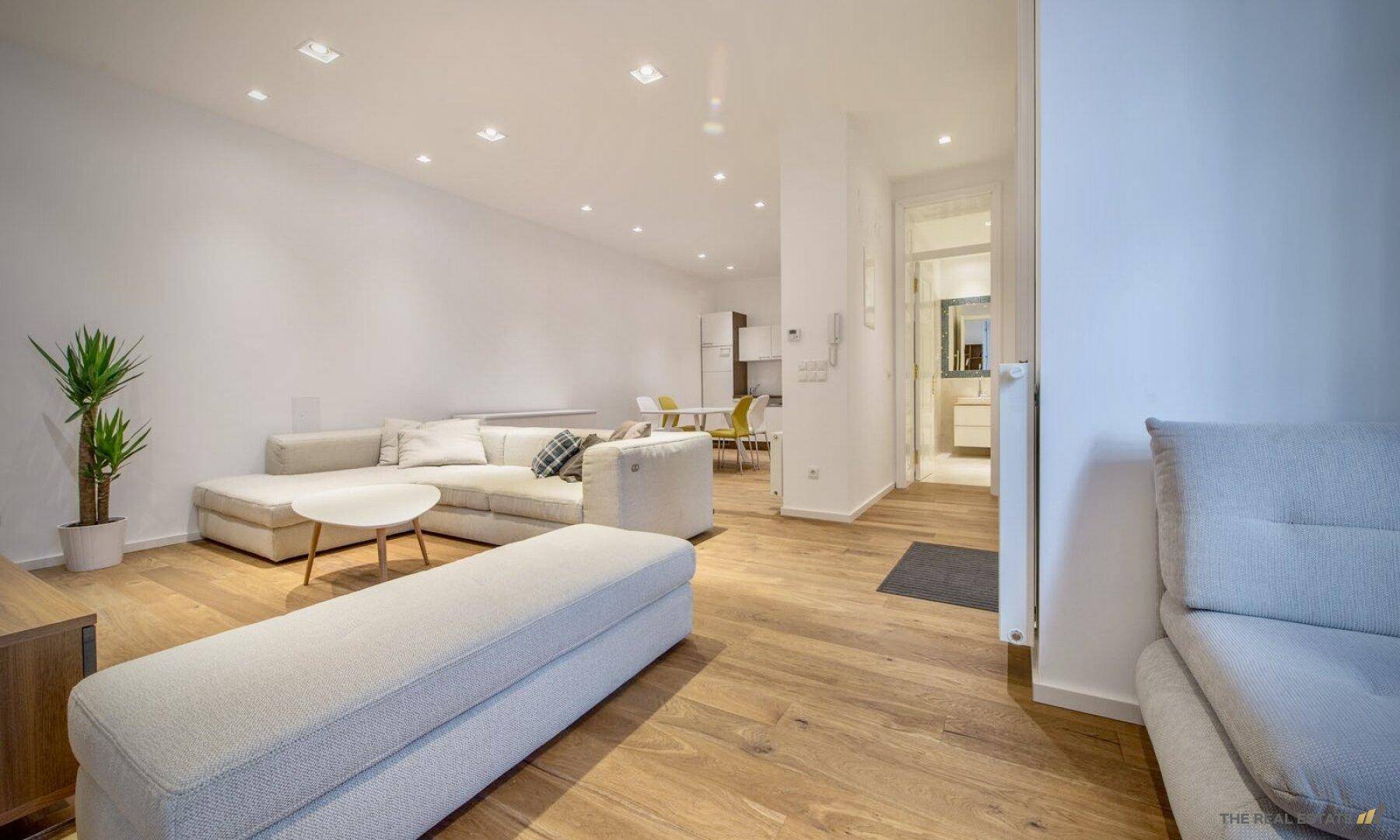 Geräumiger offener Wohnbereich mit Holzboden, moderner Einrichtung und Blick zur Küche.