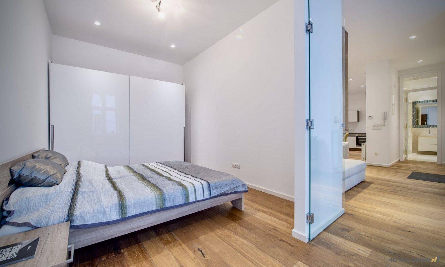 Helles Schlafzimmer mit Holzboden, Einbauschränken und direktem Zugang zum Bad.