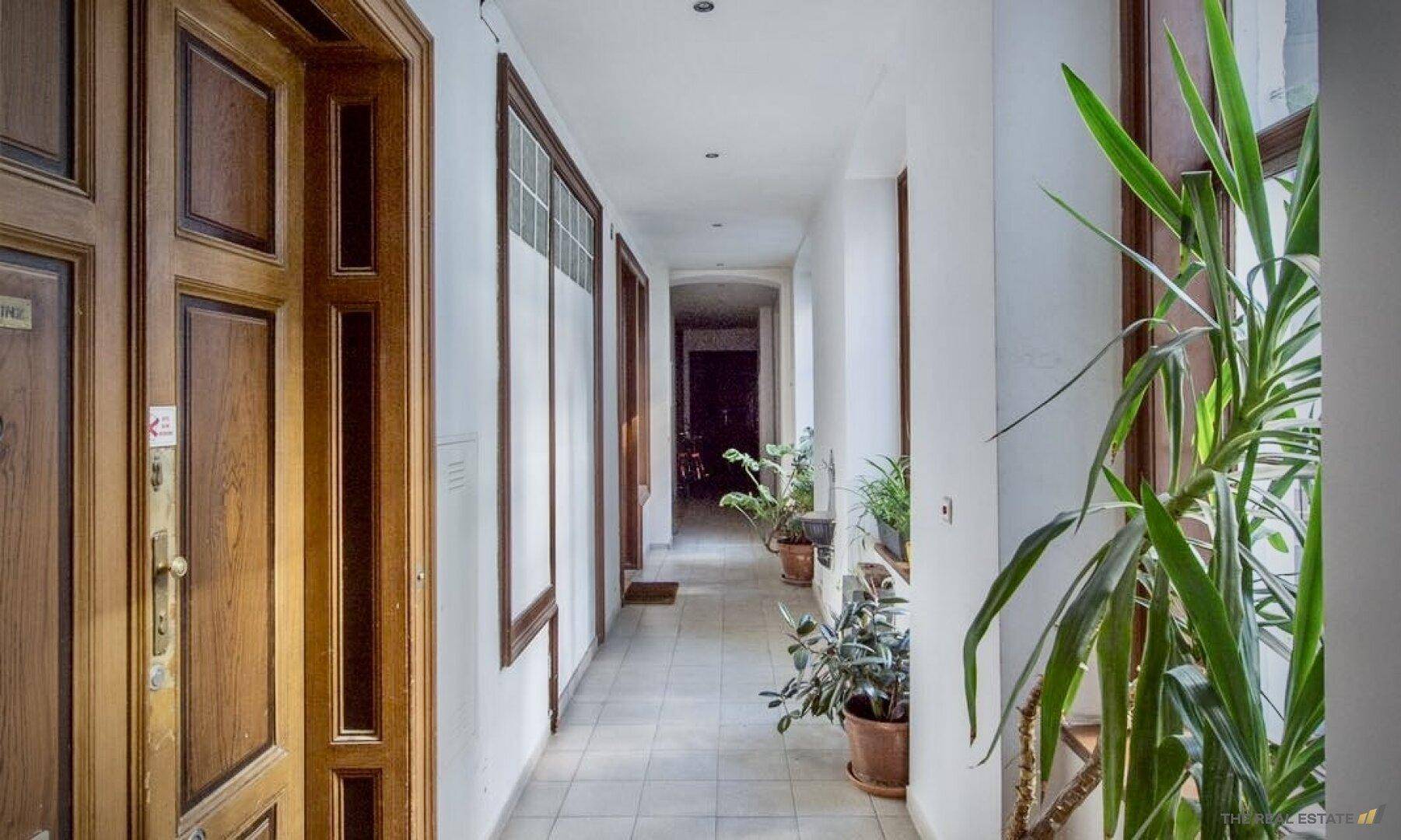 Langer Flur mit Holztüren, Fliesenboden und Pflanzen als Dekoration.