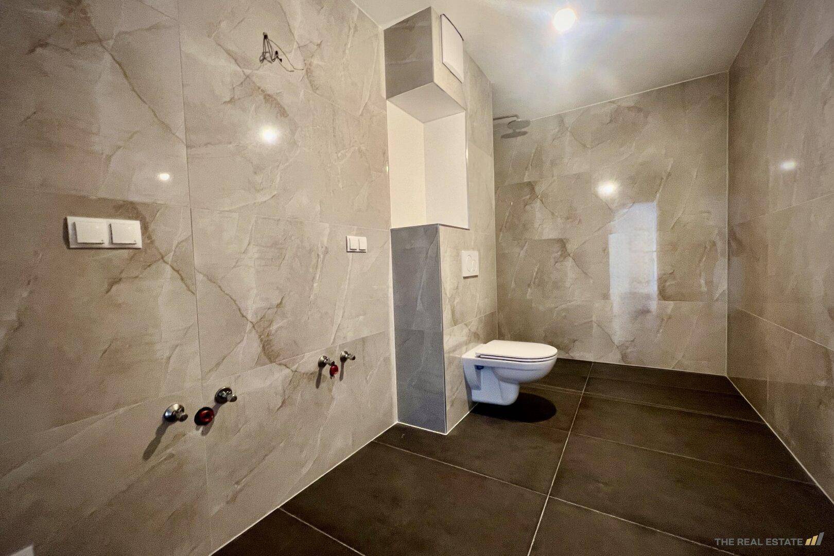 Modern gefliestes Badezimmer mit Wand-WC und Vorbereitung für weitere Sanitärinstallationen.