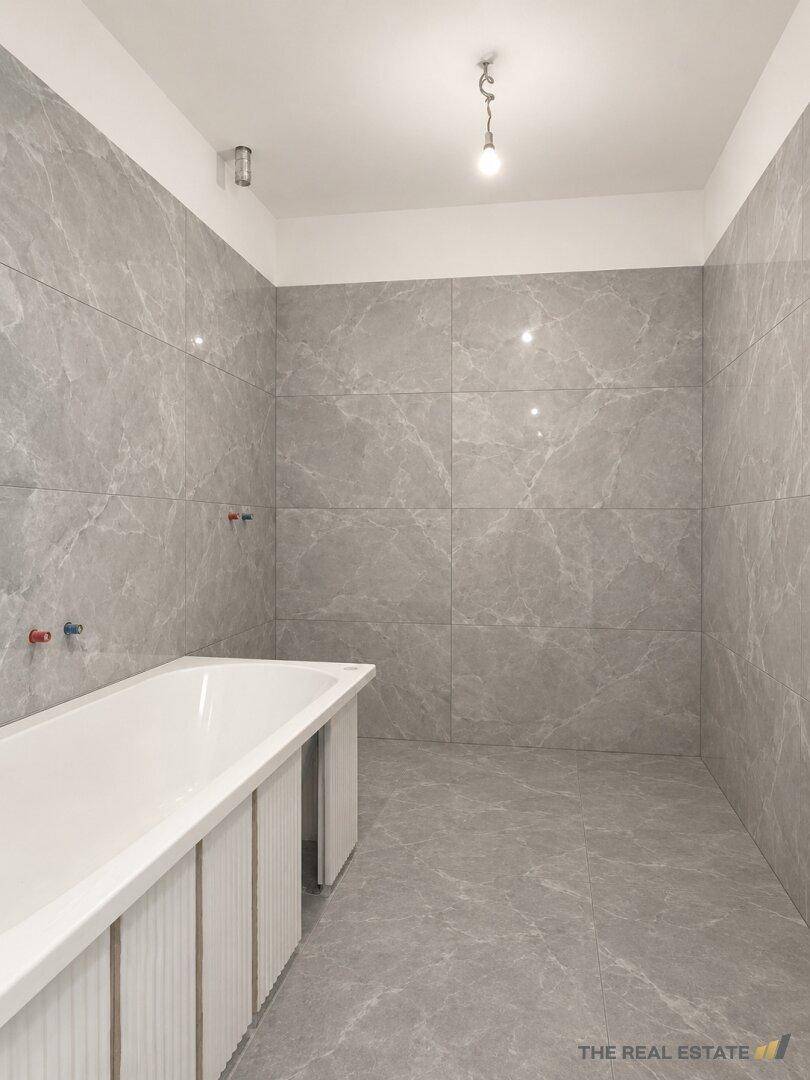 Badezimmer im Rohbau mit grauen Fliesen und eingebauter Badewanne.