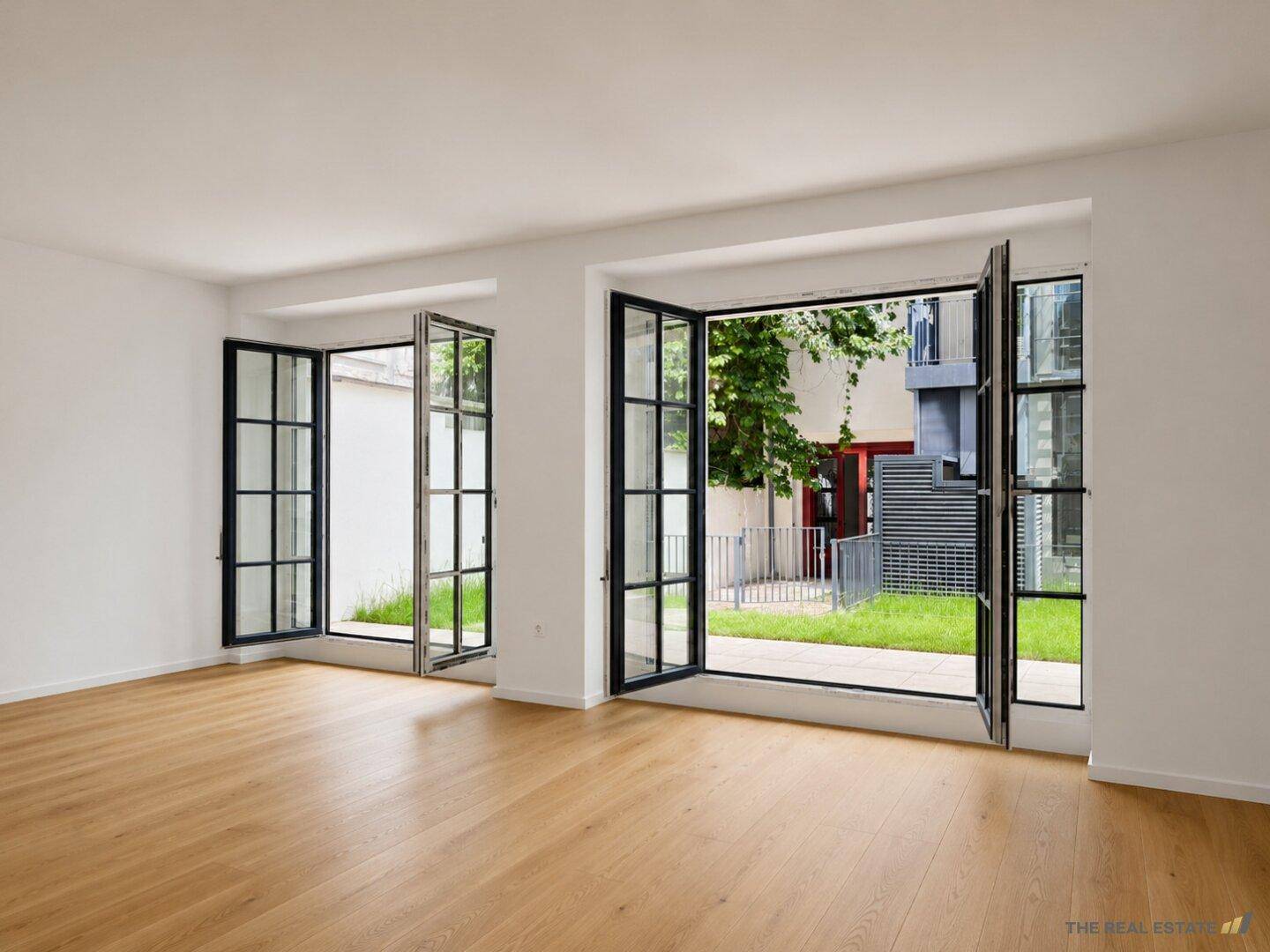 Heller Wohnraum mit Holzboden und großen Fenstertüren, die zu einem kleinen Garten führen.