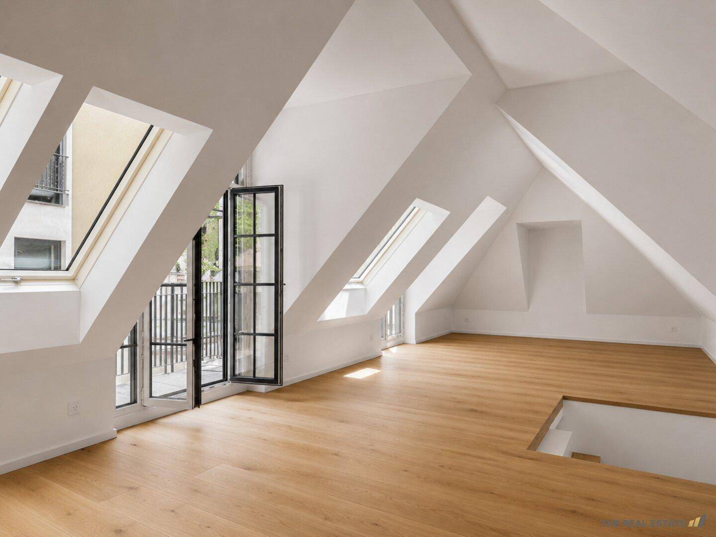 Geräumiger Dachbodenraum mit schrägen Decken, Holzboden und mehreren Dachfenstern sowie Balkonzugang.
